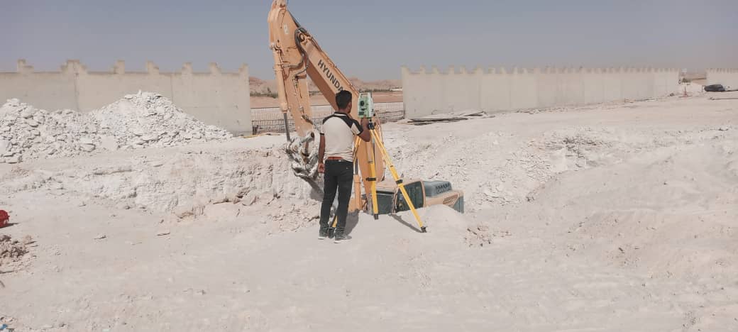 Topographe avec station totale devant une pelle Hyundai